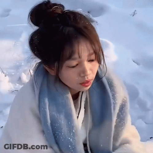 A Girl Is Sitting In The Snow With Her Eyes Closed And A Blue Scarf Around Her Neck GIF