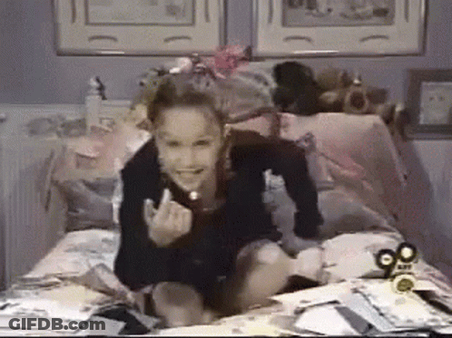 A Girl Is Sitting On A Bed With A 90.Com Logo On The Corner GIF