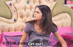 A Girl Is Sitting On A Bed With The Words Get Out Written On Her Shirt GIF
