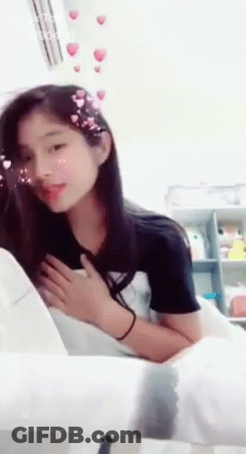 A Girl Is Sitting On A Chair With Her Hands On Her Chest GIF