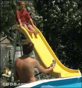 A Girl Is Sitting On A Yellow Slide In A Pool While A Man Watches GIF