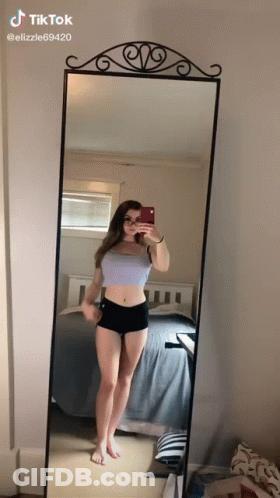 A Girl Is Taking A Selfie In Front Of A Mirror . GIF