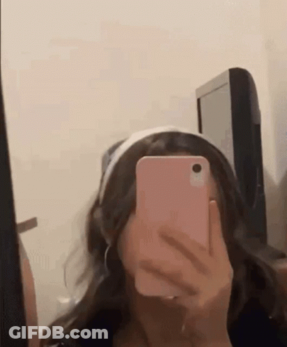 A Girl Is Taking A Selfie In Front Of A Mirror With Her Cell Phone . GIF