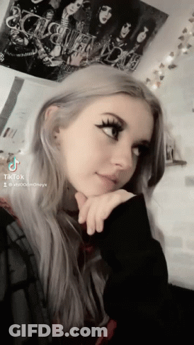 A Girl Is Taking A Selfie With A Kiss Poster Behind Her GIF