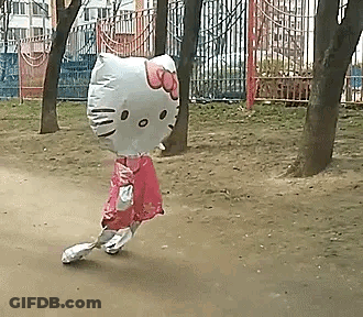 A Girl Is Walking With A Hello Kitty Balloon On Her Head In A Park . GIF