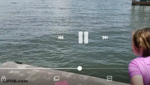 A Girl Looks Out Over A Body Of Water With A Pause Button In The Corner GIF