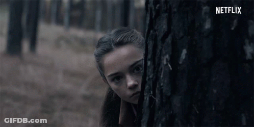 A Girl Peeking Out From Behind A Tree With The Netflix Logo In The Background GIF