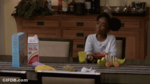 A Girl Sits At A Table With A Box Of Milk And Cereal GIF
