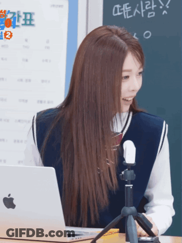 A Girl Sitting At A Desk With An Apple Laptop And A Microphone GIF