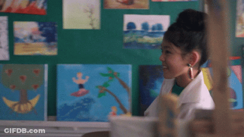 A Girl Stands In Front Of A Wall Of Paintings GIF