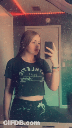 A Girl Taking A Picture Of Herself In A Mirror Wearing A Crop Top That Says Jht GIF