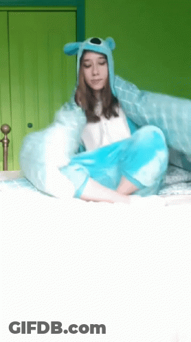 A Girl Wearing A Blue Hat And A Blue Blanket Is Sitting On A Bed GIF