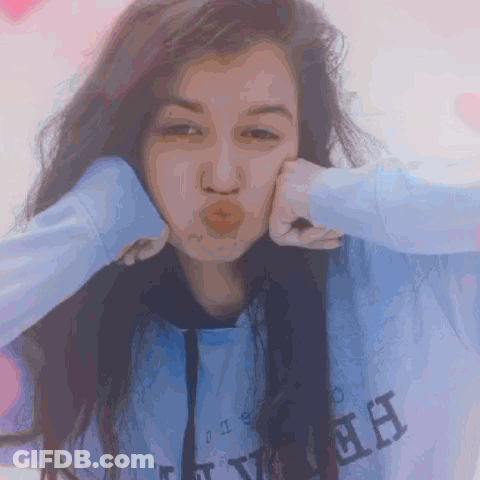 A Girl Wearing A Blue Sweatshirt With The Letter H On It Blows A Kiss GIF