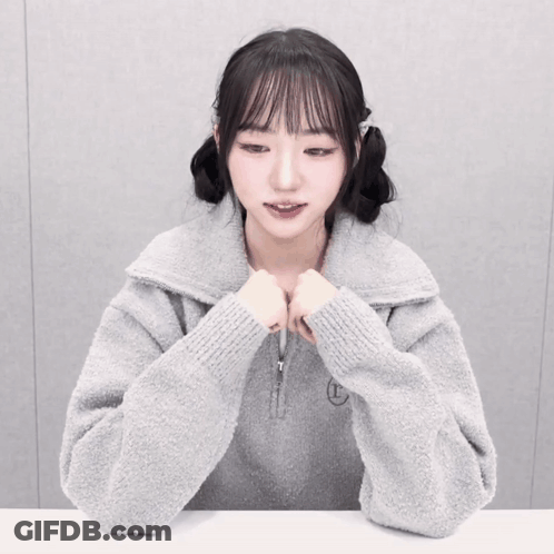 A Girl Wearing A Grey Sweater With The Letter T Embroidered On It GIF
