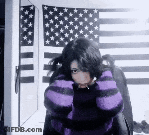 A Girl Wearing A Purple And Black Striped Sweater Is Standing In Front Of An American Flag And A Mirror . GIF