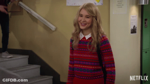 Girl In Red Sweater Smiling In Front Of Netflix Sign GIF