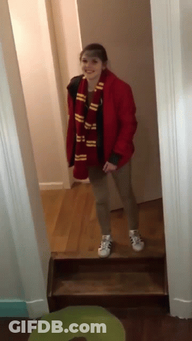 A Girl Wearing A Scarf And A Red Jacket Stands In A Hallway GIF