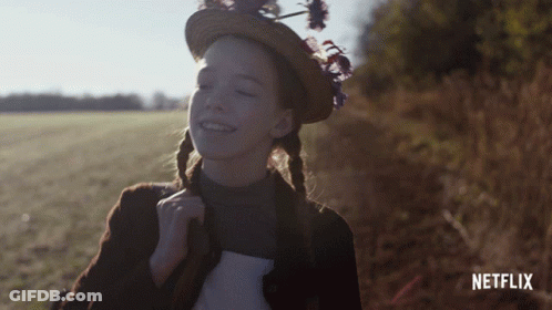 A Girl Wearing A Straw Hat With Flowers On It Is Smiling In Front Of A Netflix Logo GIF