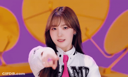 A Girl Wearing A White Jacket And A Pink Tie Points At The Camera . GIF