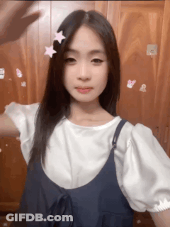 A Girl Wearing A White Shirt And Blue Overalls Has A Pink Star In Her Hair GIF