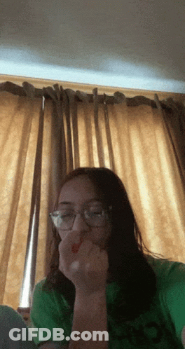 A Girl Wearing Glasses And A Green Shirt Eating A Red Strawberry GIF