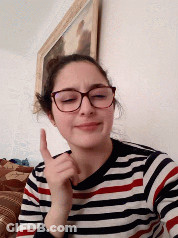A Girl Wearing Glasses And A Striped Shirt Is Giving A Thumbs Up Sign GIF