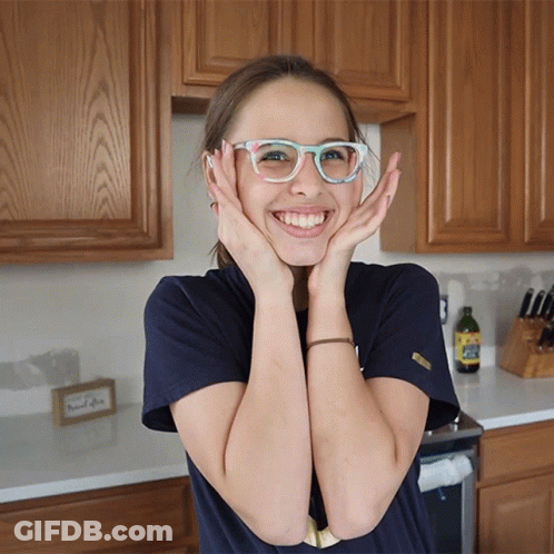 A Girl Wearing Glasses Holds Her Hands To Her Face GIF