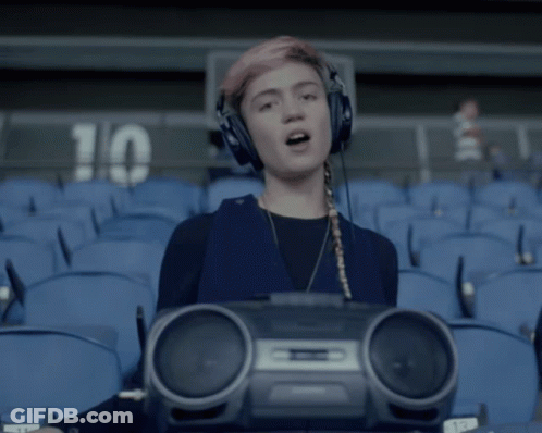 A Girl Wearing Headphones And Holding A Boombox In Front Of A Stadium With The Number 10 On The Wall GIF