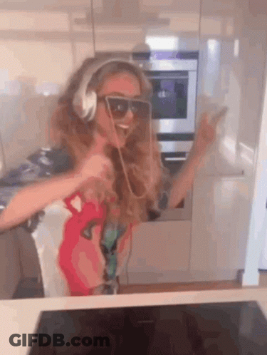 A Girl Wearing Headphones And Sunglasses Is Dancing In The Kitchen . GIF