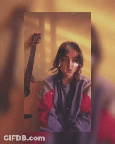 A Girl With A Bandage On Her Face Stands Next To An Acoustic Guitar GIF