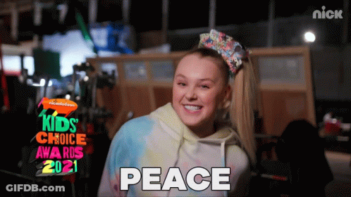 A Girl With A Bow In Her Hair Is Smiling In Front Of A Sign That Says Kids Choice Awards 2021 GIF