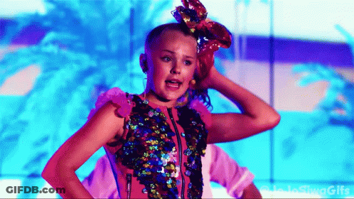 A Girl With A Bow In Her Hair Is Standing In Front Of A Blue Wall . GIF
