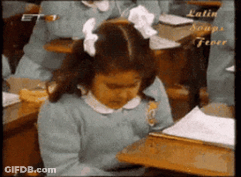 A Girl With A Bow In Her Hair Sits At A Desk In A Classroom With Latin Soups Fever Written On The Bottom GIF