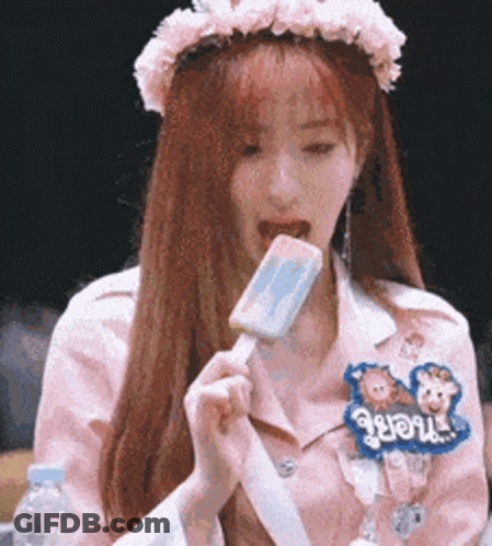 A Girl With A Flower Crown On Her Head Is Eating An Ice Cream Bar . GIF