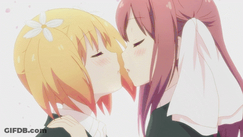 A Girl With A Flower In Her Hair Kisses Another Girl On The Cheek GIF