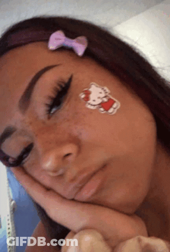 A Girl With A Hello Kitty Sticker On Her Face Rests Her Head On Her Hand GIF