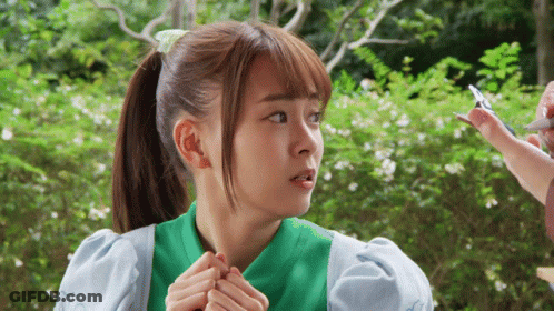 A Girl With A Ponytail And A Green Shirt Is Looking At Something GIF