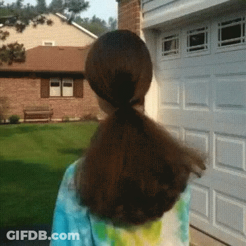 A Girl With A Ponytail Is Standing In Front Of A Garage Door GIF