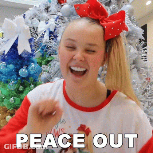 A Girl With A Red Bow In Her Hair Is Laughing In Front Of A Christmas Tree With The Words Peace Out Below Her GIF