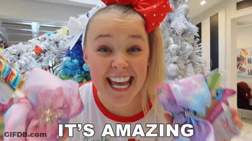A Girl With A Red Bow On Her Head Says It 'S Amazing In Front Of A Christmas Tree GIF