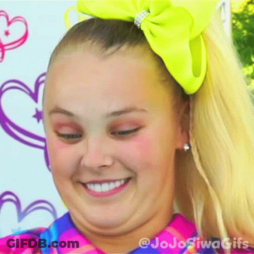 A Girl With A Yellow Bow In Her Hair Is Smiling And Making A Face . GIF