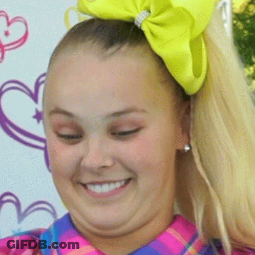 A Girl With A Yellow Bow In Her Hair Smiles For The Camera GIF