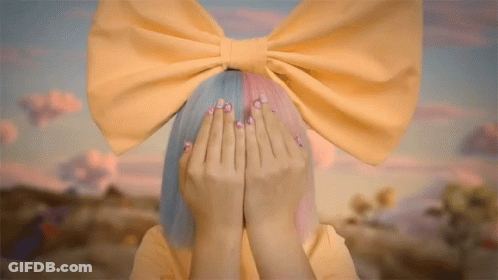A Girl With A Yellow Bow On Her Head Covers Her Face With Her Hands GIF