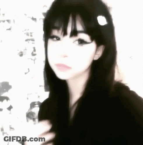 A Girl With Black Hair And Bangs Is Wearing A Black Hoodie And A Flower In Her Hair . GIF