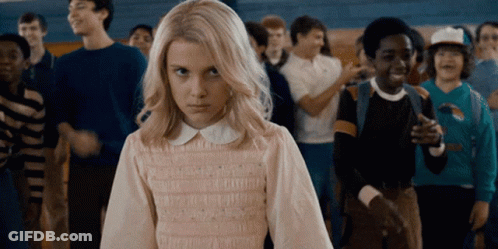 A Girl With Blonde Hair Is Standing In Front Of A Crowd Of People GIF