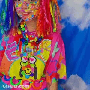 A Girl With Colorful Hair And Face Paint Is Wearing A Colorful Shirt And Necklaces . GIF