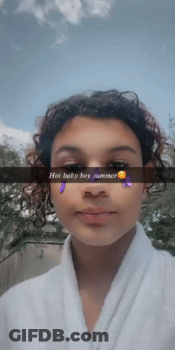 A Girl With Curly Hair Is Wearing A White Robe And A Snapchat Filter That Says Hot Baby Boy Summer GIF