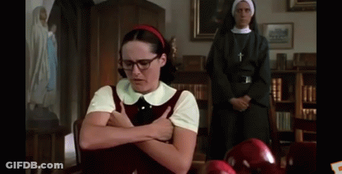 A Girl With Glasses And A Red Headband Is Sitting At A Table With Her Arms Crossed In Front Of A Nun . GIF
