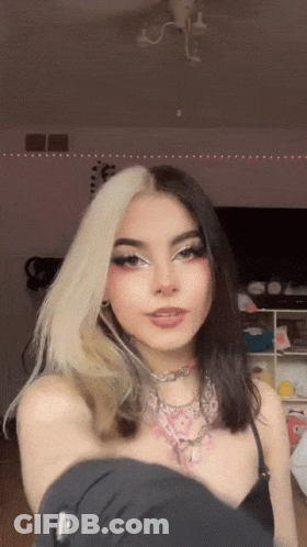 A Girl With Half White And Half Black Hair Is Taking A Selfie In A Room . GIF