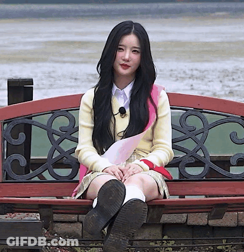 A Girl With Long Black Hair Is Sitting On A Bench With Her Legs Crossed GIF